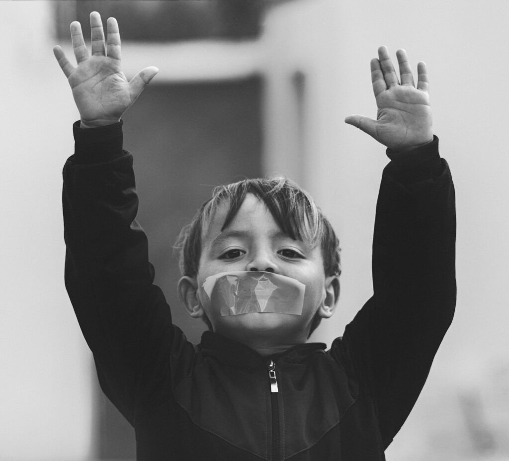 A child with tape on mouth raises hands, conveying a powerful silent message.